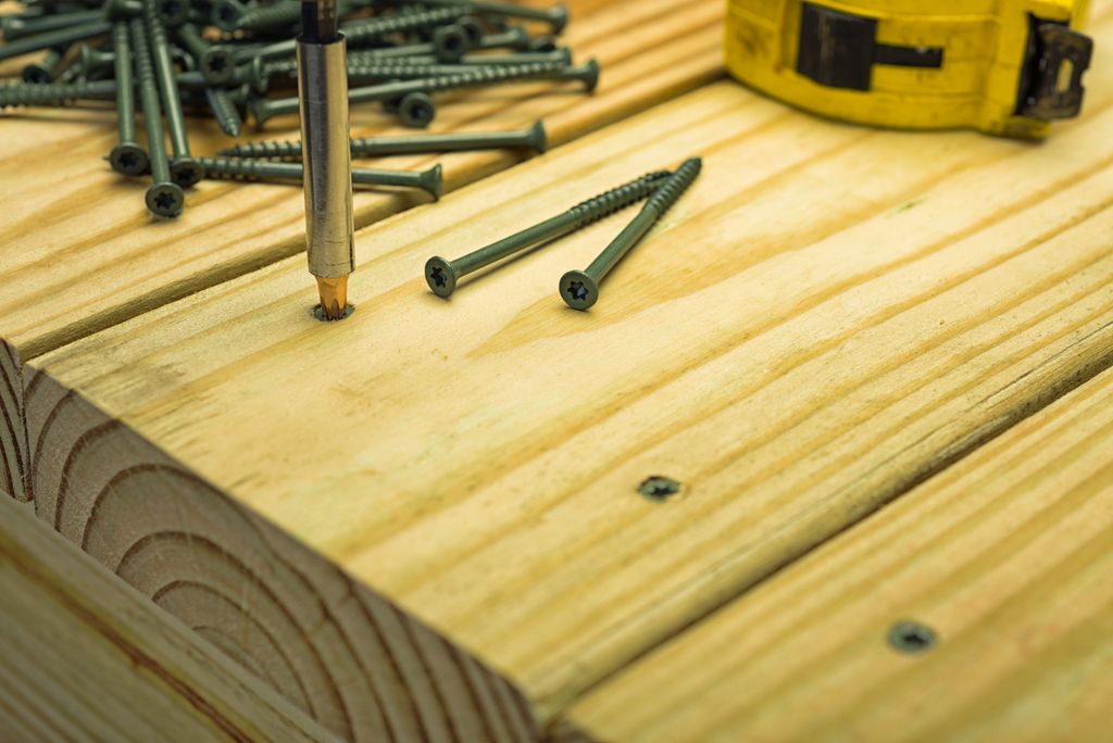 A power drill driving coated screws into a pressure treat 2x6 deck boards.